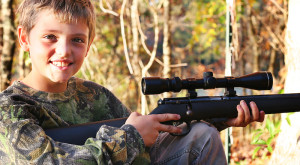 little boy hunting with a gun smile